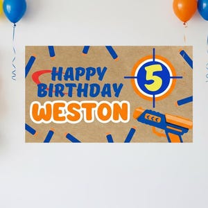 May include: A birthday banner with the text "Happy Birthday Weston" in blue and orange. The number "5" is in a target design. A toy gun is also featured. Balloons in yellow, blue, and orange are in the background.