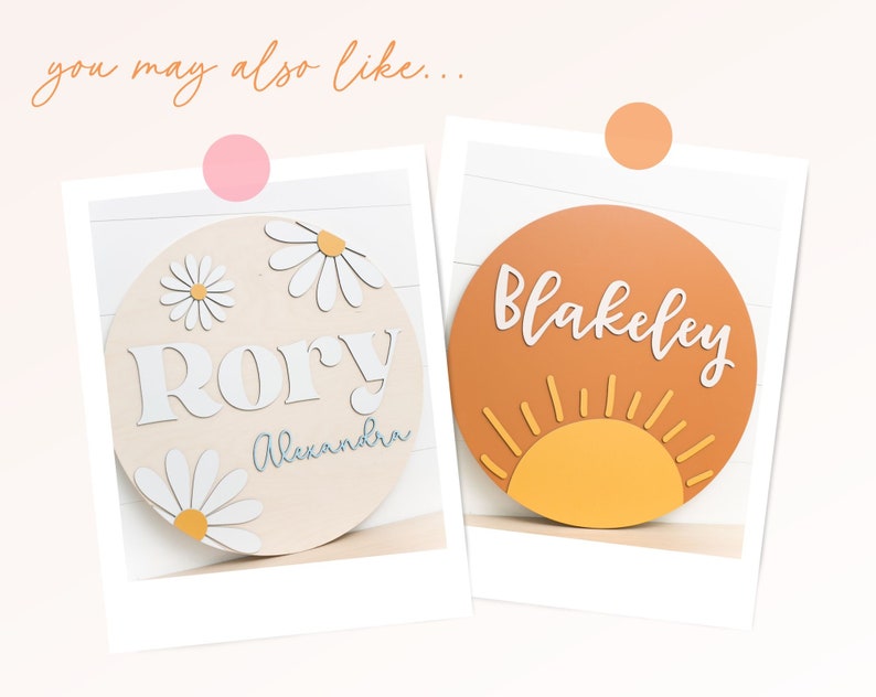 Puede incluir: Dos letreros redondos de madera con nombres personalizados. El primer letrero es de madera clara con margaritas blancas y el nombre "Rory Alexandra". El segundo letrero es naranja con un sol amarillo y el nombre "Blakeley".