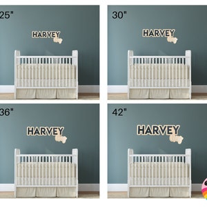 May include: Four images showing a crib with a wooden name sign above it. The name sign says "HARVEY". The crib is white with a white mattress and white bedding. The name sign is on a blue wall. The images show the name sign at different heights above the crib: 25 inches, 30 inches, 36 inches, and 42 inches.