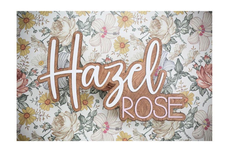 May include: Wooden sign with the name "Hazel Rose" in a layered design. The top layer is white, and the bottom layer is a light brown wood. The word "Rose" is outlined in pink. The background is a floral pattern.