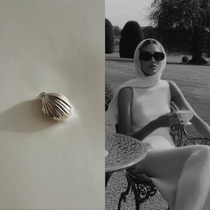 May include: A silver seashell-shaped pendant. The pendant has a ridged texture and is set against a white background. A person wearing sunglasses and a white dress is seated outdoors, holding a teacup.