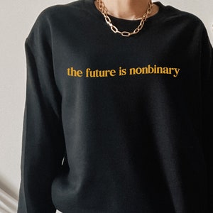 Op de afbeelding: Een zwart sweatshirt met de tekst "the future is nonbinary" in gouden letters.