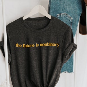 May include: A dark grey t-shirt with the text "the future is nonbinary" in yellow lettering.