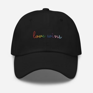 May include: Black baseball cap with the text "love wins" embroidered in rainbow colors.