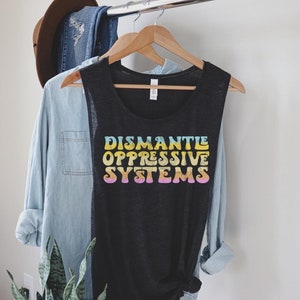 May include: A black sleeveless muscle tank top with the text "DISMANTLE OPPRESSIVE SYSTEMS" printed in rainbow colors.