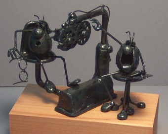 May include: A whimsical metal sculpture depicting a dentist examining a patient. The dentist and patient are both made of wire and metal, and the dentist is holding a dental tool. The sculpture is mounted on a wooden base.
