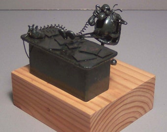 May include: A metal sculpture of a person sitting at a desk, talking on the phone. The sculpture is on a wooden base.