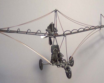May include: A model of a small aircraft made from metal, with a propeller and wheels. The aircraft is suspended by wires and appears to be in flight.