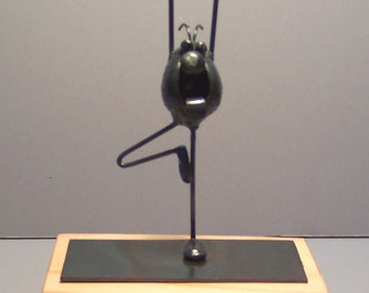 May include: A metal sculpture of a person doing yoga on a wooden base with a black metal top.