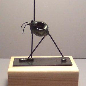 May include: A black metal sculpture of a person with one arm raised in the air. The sculpture is standing on a wooden base.