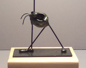 May include: A black metal sculpture of a person with one arm raised in the air. The sculpture is standing on a wooden base.