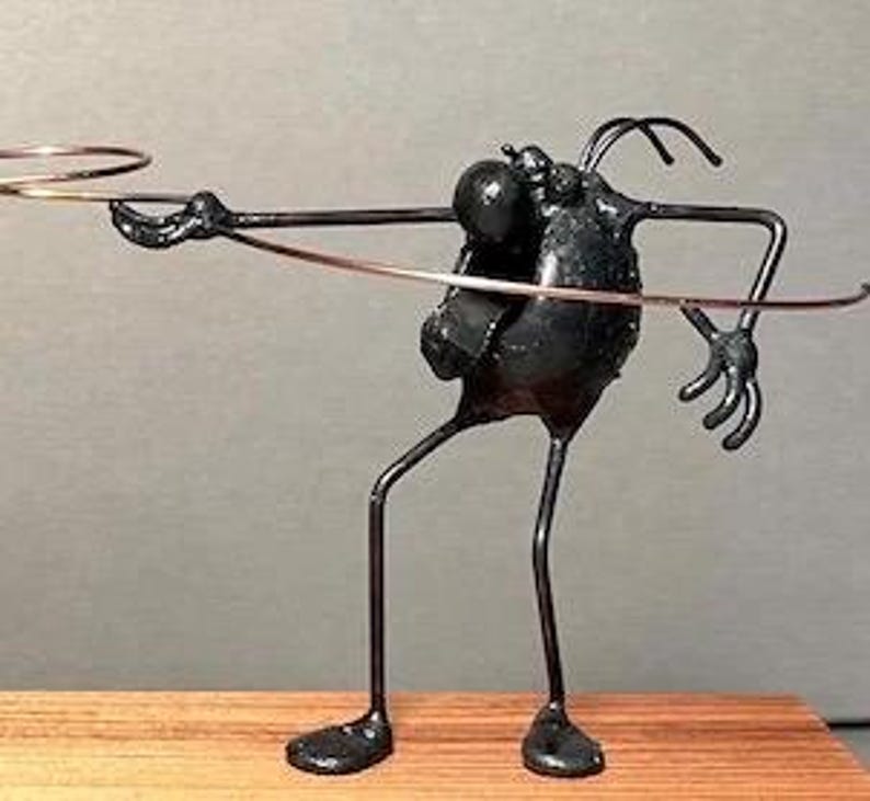 May include: A black metal sculpture of a stylized figure with long limbs and a round head. The figure is holding a ring in its outstretched hand.