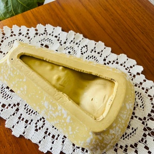 May include: A yellow ceramic ashtray with white speckles. The ashtray is shaped like a triangle with a rounded bottom. The inside of the ashtray is empty.