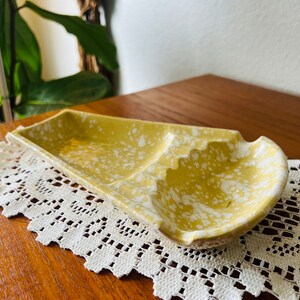 May include: A yellow ceramic ashtray with white speckles. The ashtray has two compartments for cigarettes.
