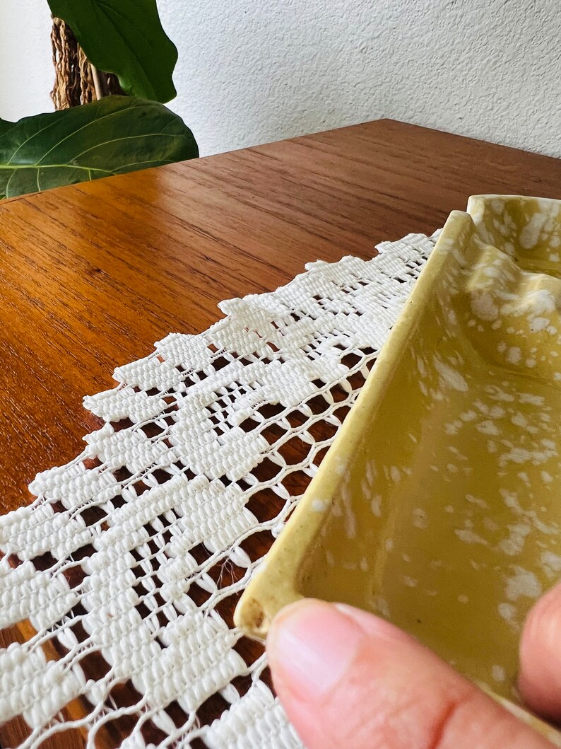 May include: A yellow ceramic ashtray with white speckles. The ashtray has a rectangular shape with rounded edges.