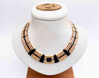 Puede incluir: Un collar de oro con eslabones rectangulares rayados en negro, blanco y naranja. El collar tiene una piedra negra cuadrada en el centro.