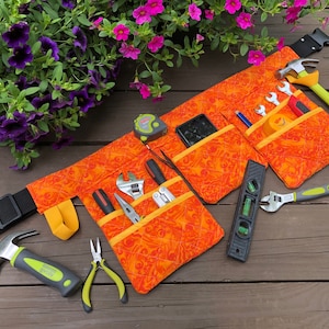 May include: Orange and yellow tool belt with multiple pockets and a variety of tools including a hammer, pliers, a spirit level, a tape measure, and a wrench.