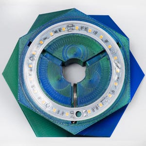 Peut inclure: Une base hexagonale en impression 3D bleue et verte avec un anneau de LED blanches autour du trou central.