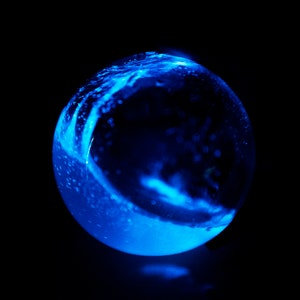 May include: A glowing blue glass sphere against a black background. The sphere has a swirling, liquid-like pattern with bright highlights, creating a dynamic and ethereal effect. The overall aesthetic is futuristic and abstract.