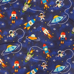 May include: A blue fabric with a repeating pattern of rockets, astronauts, stars, and planets. The pattern is in shades of blue, white, and red.