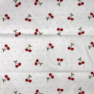 May include: White fabric with a repeating pattern of red cherries and green leaves. The cherries are scattered across the fabric, interspersed with small black dots. The fabric appears to be cotton or a similar material.