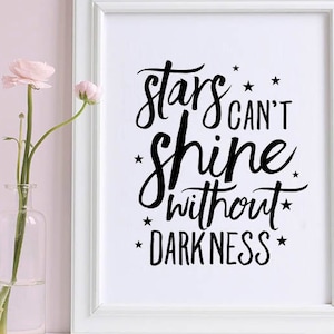 May include: A white framed print with the text "stars can't shine without darkness" in black script. The print is next to three clear glass vases with pink flowers. The background is a light pink wall.