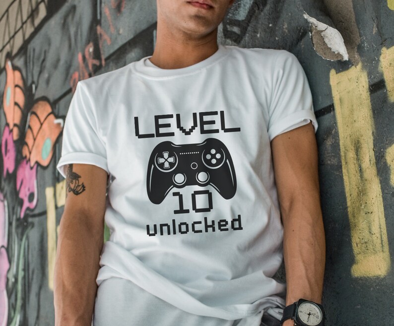 May include: White t-shirt with a black video game controller graphic and the text "LEVEL 10 unlocked" in a pixelated font.
