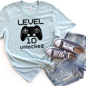 May include: A light blue t-shirt with a black graphic of a video game controller and the text "LEVEL 10 unlocked".