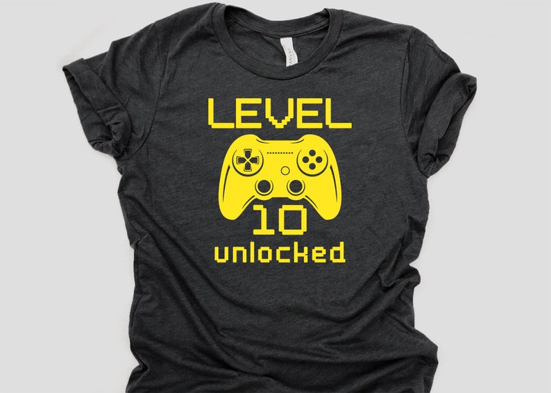 May include: A dark gray t-shirt with a yellow graphic of a video game controller and the text "LEVEL 10 unlocked".