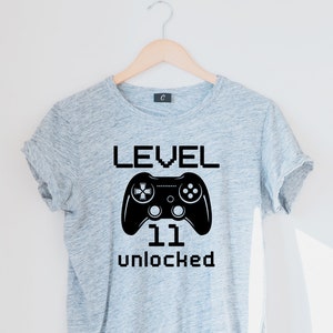 May include: Gray t-shirt with a black video game controller graphic and the text "LEVEL 11 UNLOCKED".