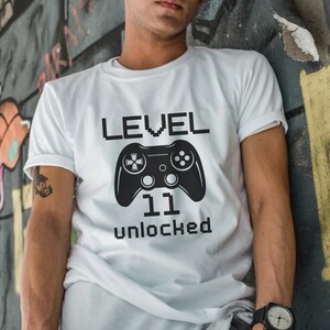 May include: White t-shirt with a black video game controller graphic and the text "LEVEL 11 unlocked".