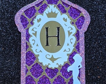 May include: Purple glitter card with a gold frame and the letter "H" inside. The frame has a crown on top and a silhouette of a woman in a flowing robe on the right side.