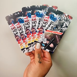 Puede incluir: Una pila de tarjetas coloridas con la palabra "REBEL" impresa en ellas. Las tarjetas tienen un collage de im&aacute;genes, incluyendo un tigre, la cara de una persona y el texto "Have something to talk about".