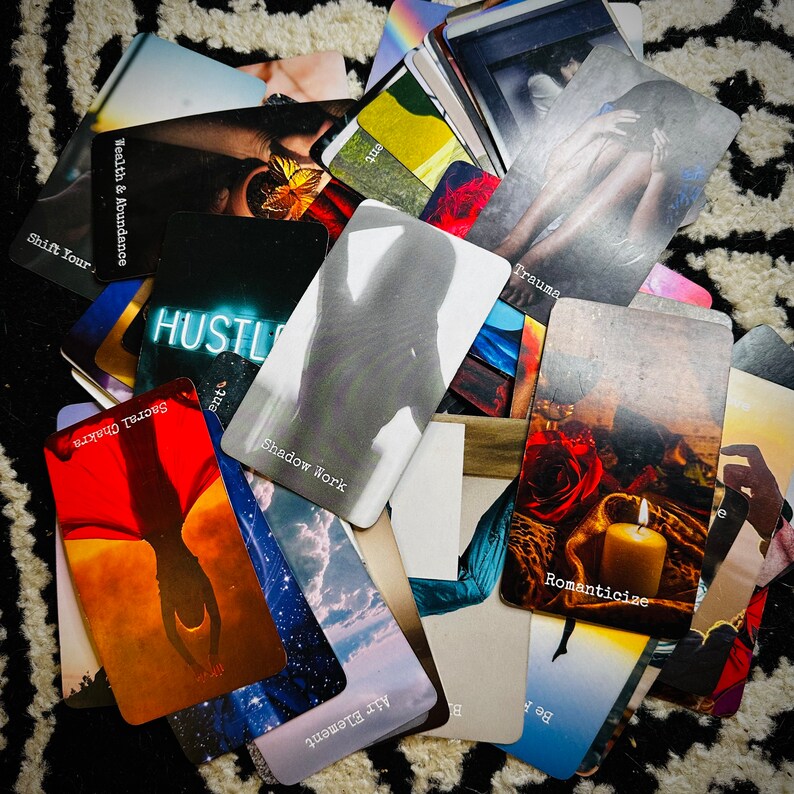 Puede incluir: Una colecci&oacute;n de cartas de or&aacute;culo con varios temas, incluyendo "Wealth & Abundance", "Shift Your", "Hustle", "Sacral Chakra", "Trauma", "Shadow Work", "Romanticize", "Air Element", y "Be".