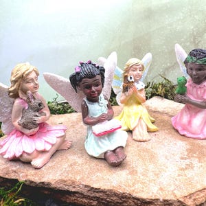 Op de afbeelding: Vier fee-figuurtjes met vleugels, elk met een ander dier. De feeën dragen roze, gele en blauwe jurken. De feeën zitten op een rots.