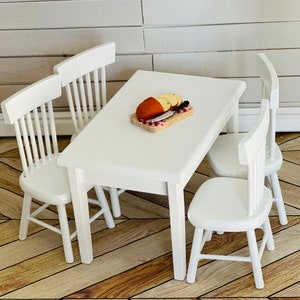 May include: A white table with four white chairs. The table has a wooden cutting board with a knife and sliced bread on it.