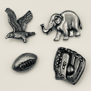 May include: Four pewter figurines: a bird, an elephant, a football, and a baseball glove. The figurines are all silver in color and have a detailed design.