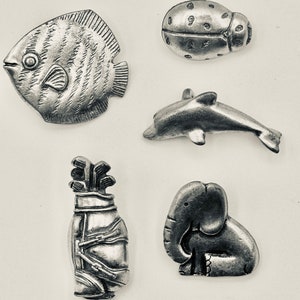 May include: Five pewter figurines: a fish, a ladybug, a dolphin, a golf bag, and an elephant. The figurines are all in a silver colour and have a detailed design.