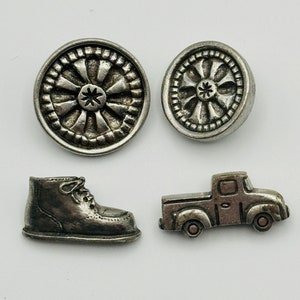 Könnte beinhalten: Vier silberfarbene Metallknöpfe mit verschiedenen Designs. Die Knöpfe zeigen ein Rad, einen Stiefel, einen LKW und ein weiteres Rad.