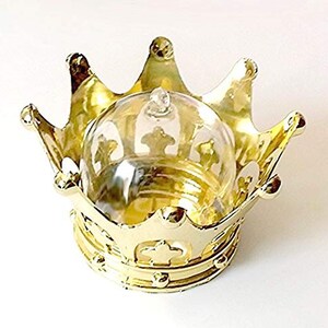 Puede incluir: Un recipiente dorado en forma de corona con una c&uacute;pula de cristal transparente. La corona tiene detalles ornamentados y un acabado brillante. La c&uacute;pula de cristal tiene un peque&ntilde;o pomo en la parte superior y est&aacute; dise&ntilde;ada para encajar en la corona.