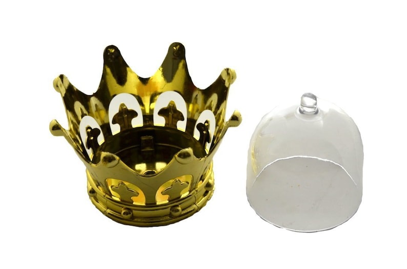 Puede incluir: Un portavelas dorado en forma de corona con una tapa transparente en forma de c&uacute;pula. La corona tiene un dise&ntilde;o decorativo con formas recortadas. La tapa tiene un peque&ntilde;o asa en la parte superior. Art&iacute;culos para la decoraci&oacute;n del hogar.