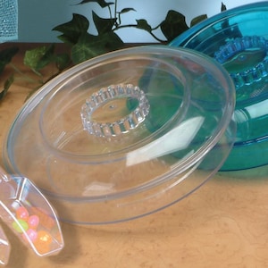May include: Clear plastic hamster wheel with a clear plastic ring in the center. A second, teal-colored wheel is visible in the background. A small scoop with colorful balls is in the foreground.