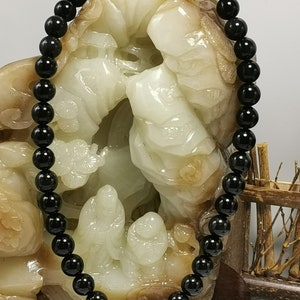 May include: A black beaded necklace made of round, smooth beads. The necklace is draped over a white jade sculpture.