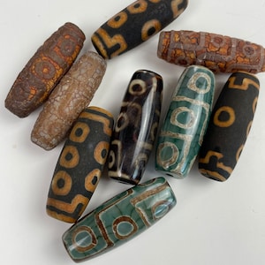 May include: A collection of eight agate beads with various patterns and colours, including brown, black, green, and white. The beads are oval-shaped and have a smooth, polished finish.
