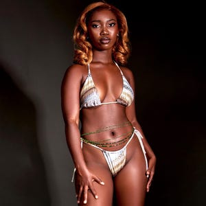 K&ouml;nnte beinhalten: Eine Frau tr&auml;gt ein wei&szlig;-braunes gemustertes Bikinioberteil und einen passenden Slip mit einer gr&uuml;nen Perlenkette um die Taille.
