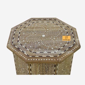 May include: An octagonal wooden table with intricate floral inlay designs. The table features a light brown finish with white and black accents. The top and sides showcase detailed patterns, creating a decorative piece.
