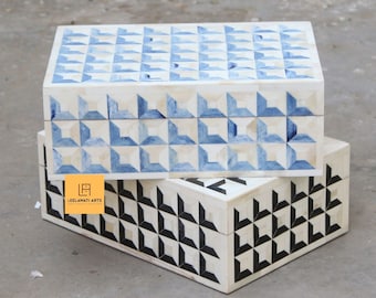 May include: Two decorative boxes with geometric patterns. The top box has a blue and white pattern, while the bottom box has a black and white pattern. Both boxes are made of bone inlay.