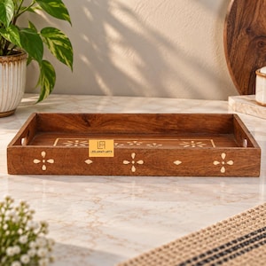 May include: A rectangular brown wooden serving tray featuring light-colored floral inlay patterns on the front side and interior base. A small yellow rectangular label with the black text LEELAWATI ARTS is attached to the center of the tray.