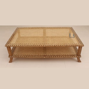 Pode incluir: Uma mesa de centro retangular com tampo de palhinha natural e prateleira inferior. A estrutura de madeira &eacute; decorada com padr&otilde;es incrustados complexos ao longo das bordas e apoiada por quatro pernas curvas. O texto LA LILA ARTS &eacute; vis&iacute;vel.