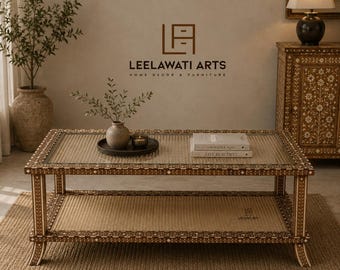 Pode incluir: Uma mesa de centro retangular com tampo de vidro e prateleira inferior trançada, apresentando intrincados padrões de incrustação floral em marrom e branco na estrutura e nas pernas. A mesa é decorada com um pequeno vaso, uma vela e dois livros.